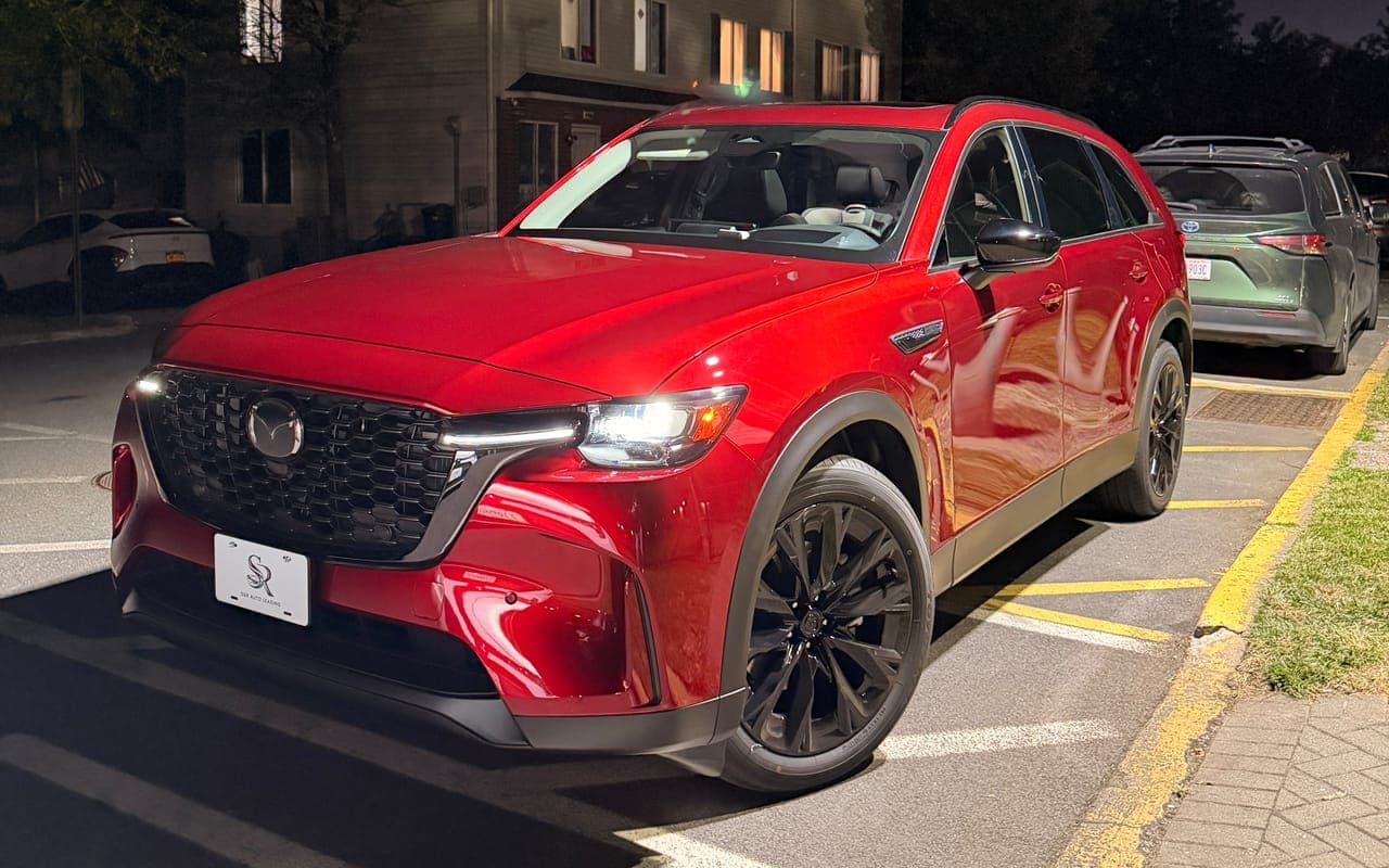 A red Mazda CX-90 with black wheels and an S&R plate, seen from the front in a parking lot